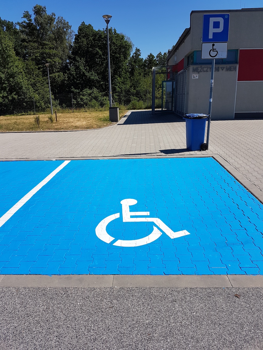 koperta dla osoby z niepełnosprawnością pomalowana na niebiesko z białym symbolem P-24 na parkingu z kostki brukowej
